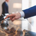 Mão de homem com terno apertando o sino de recepção de hotel
