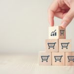 Cubos de madeira estampados com carrinho de compras empilhados com uma mão colocando mais um por cima dos demais