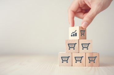 Cubos de madeira estampados com carrinho de compras empilhados com uma mão colocando mais um por cima dos demais