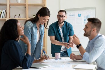 2 colaboradores homens e 2 colaboradoras mulheres estão sorrindo e conversando ao redor de uma mesa